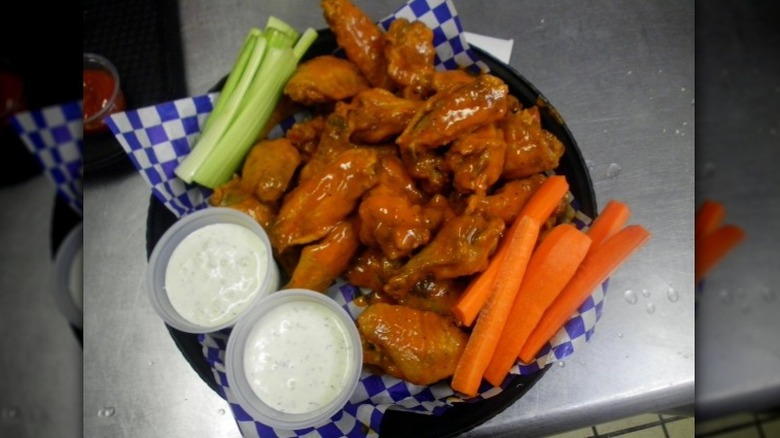 A plate of buffalo chipotle garlic chicken wings sits on a metal table