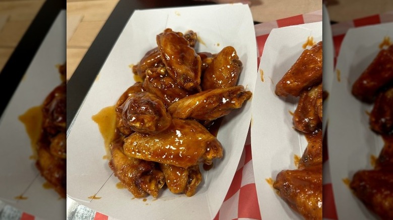 Sauced chicken wings sit in a paper boat on a black table