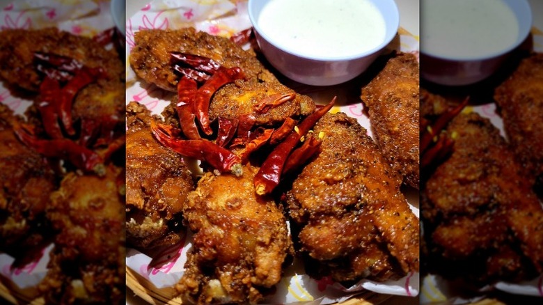 Spicy chicken wings with red chilies sit in a paper lined basket with a dipping sauce