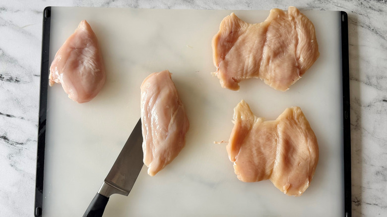 Knife slicing into chicken breast next to butterflied chicken breasts on cutting board