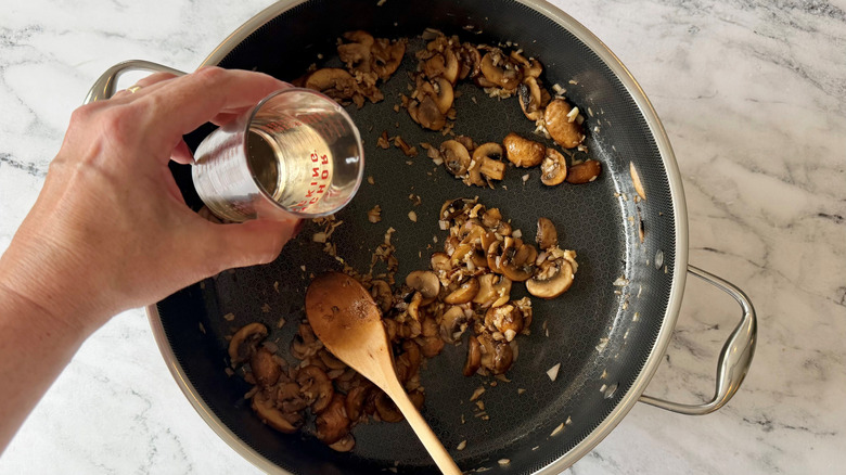 Hand pouring white wine into pan with mushrooms