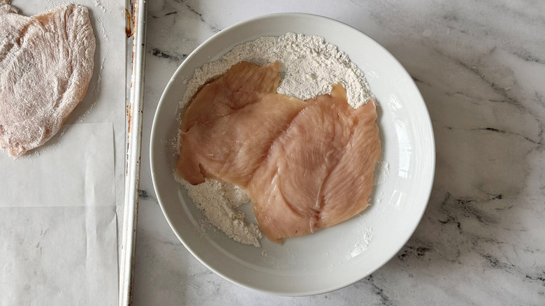 Butterflied chicken breast in bowl of flour