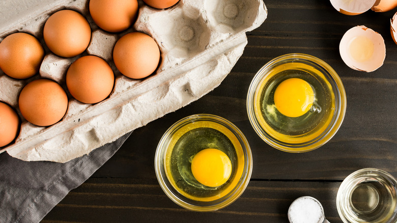 A carton of eggs and two cracked eggs in ramekins