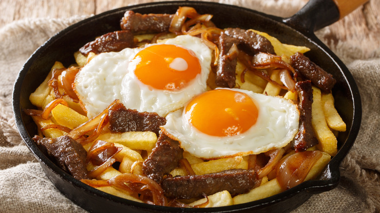 A skillet of chorrillana with caramelized onions and sunny eggs