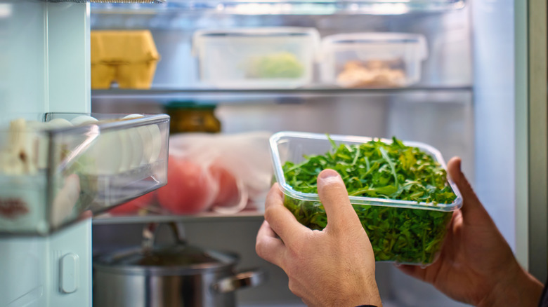 Person storing a tub of greens in the fridge.