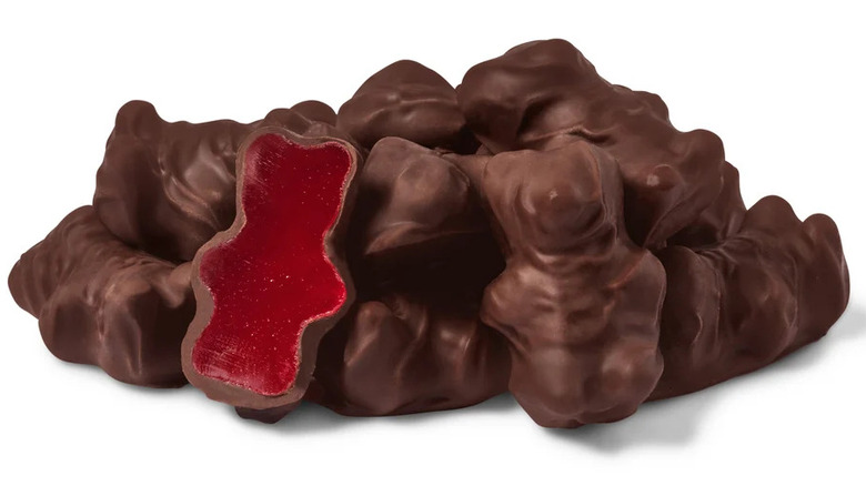 A pile of chocolate-covered cinnamon bears, with half the chocolate shell removed from one, showing the gummy underneath