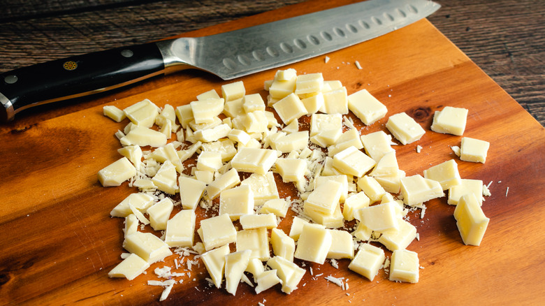 A white chocolate bar chopped into chunks on a wood cutting board with a chef's knife in the background