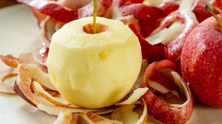 Peeled apple surrounded by red apple peels