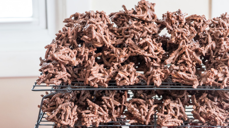 A cooling rack is stacked tall with chocolate haystack cookies
