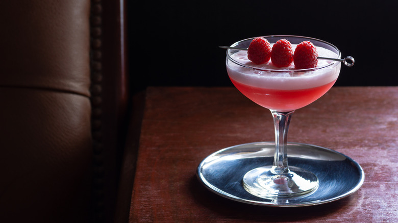 A clover club cocktail on a small silver plate on a wooden table