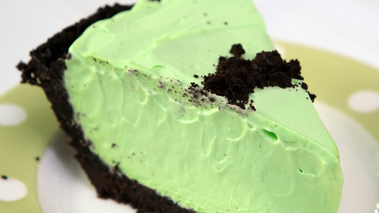 Cookie crumb topped slice of mint green grasshopper pie before a black and white napkin