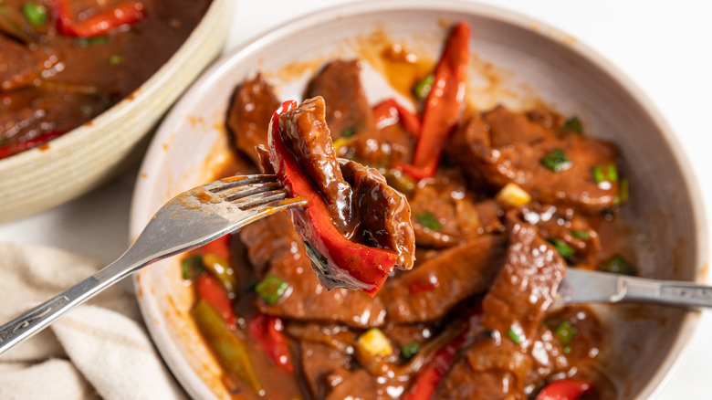 Fork with piece of meat and red bell pepper over a plate with pepper steak