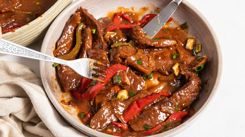 Dish with slices of steak, red and green bell pepper, and green onion mixed in brown sauce