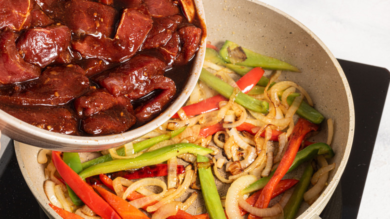 Marinated meat added to a skillet with cooked veggies