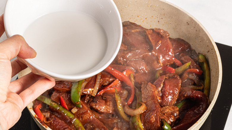 Adding cornstarch slurry to a skillet with meat and veggies