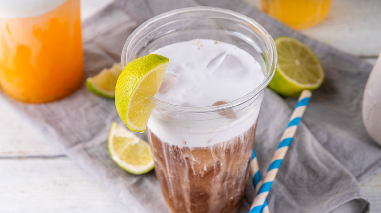 A homemade dirty soda in a clear plastic cup with a wedge of lime