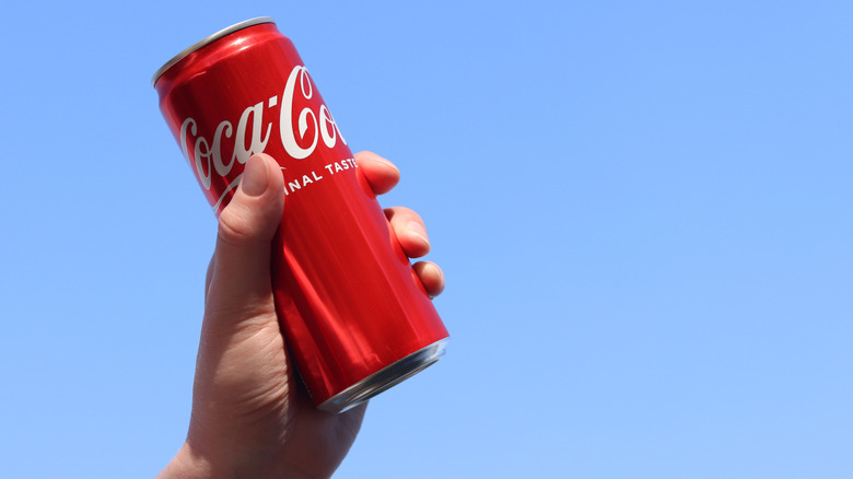 A can of Coca Cola held aloft against a blue sky.