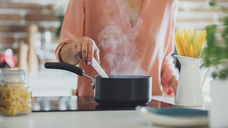 A woman stirring a small pot of boiling water with different pastas handy
