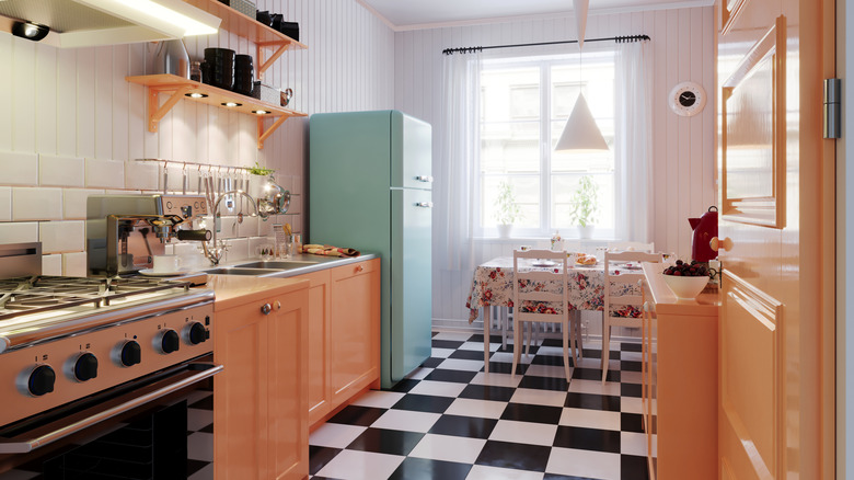 A vintage style kitchen with a colorful fridge, black and white floor and simple wood cabinets