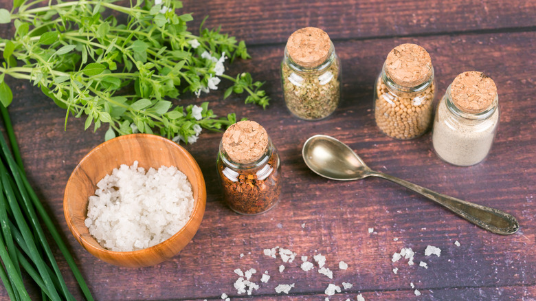 A bowl of salt, as well as spices and herbs, sit on a wooden surface