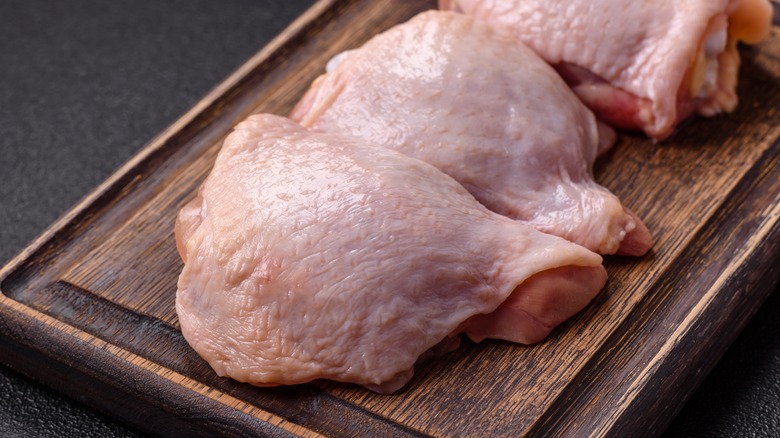 Raw skin-on chicken thighs sit on a wooden cutting board