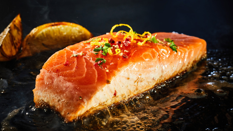 Salmon cooking on a griddle next to lemon wedges.