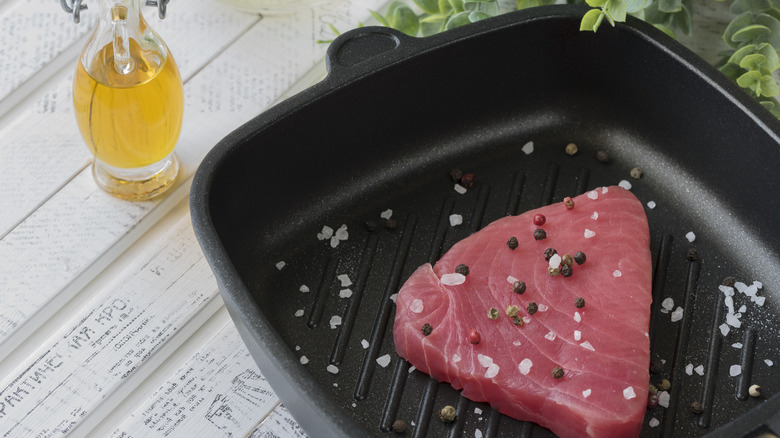 Seasoned tuna fillet in a pan next to a jar of cooking oil.
