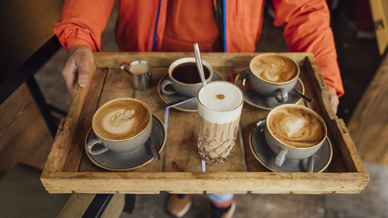 A person holding a tray with several different types of coffee.