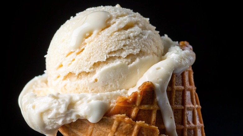 A scoop of dripping vanilla ice cream in a waffle cone