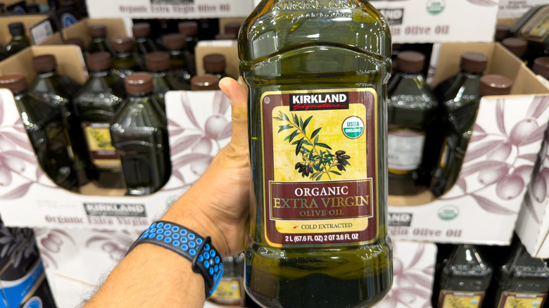 Hand holding a large jug of Kirkland Signature Olive Oil