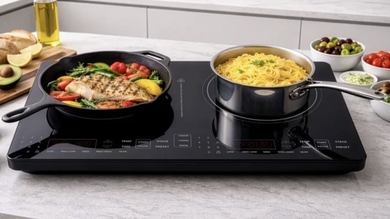 Cookware with a prepared meal atop a Nuwave cooktop on a kitchen counter surrounded by ingredients