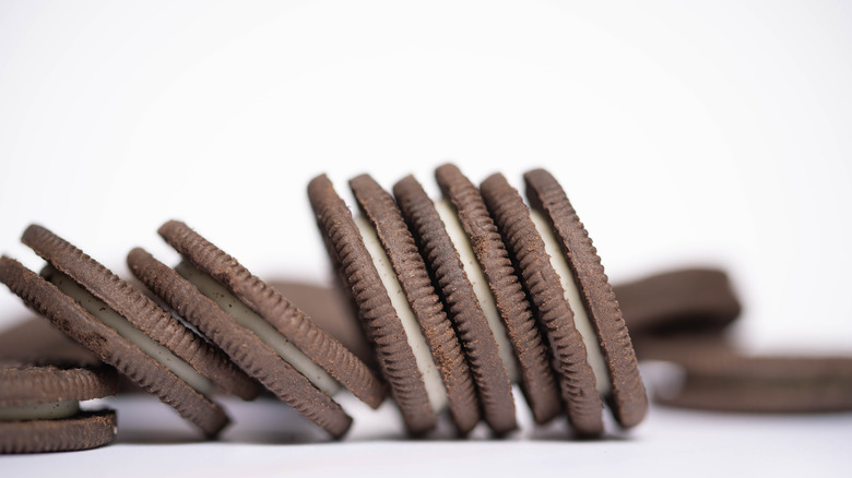 Oreo cookies on a white table stacked upright and leaning over like dominoes.