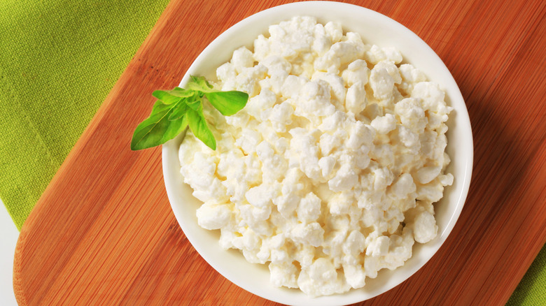 cottage cheese in a white bowl on wooden cutting board with a fresh herb in it