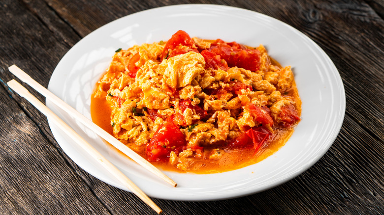 Chopsticks on plate of tomato and egg omelette