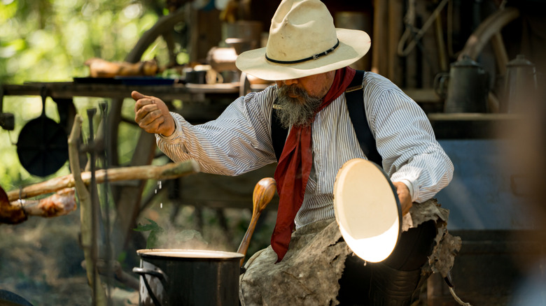 A cowboy is cooking a meal over an open fire.