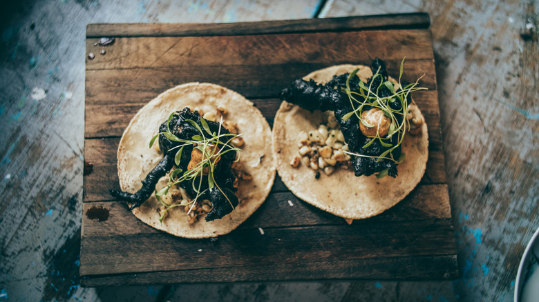 Two rustic soft tacos containing organ meat sit on a wooden surface.