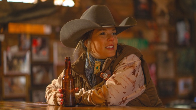 Western-garbed person in a cowboy hat drinking from a bottle at a bar.