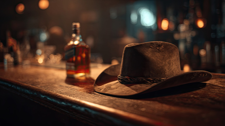 A cowboy hat on a bar next to a bottle.