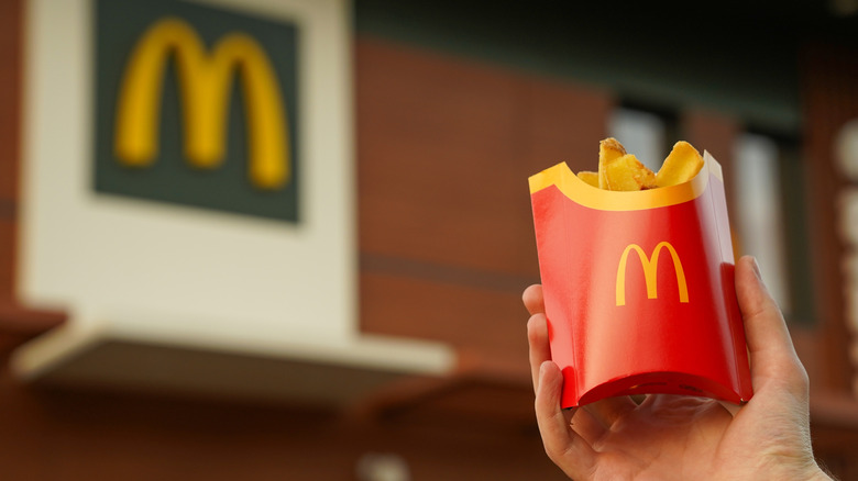 A hand holds a container of McDonald's french fries outdoors in closeup