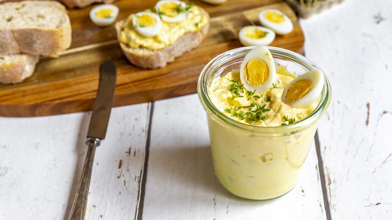 Cup of creamy egg salad on white table with bread in the background
