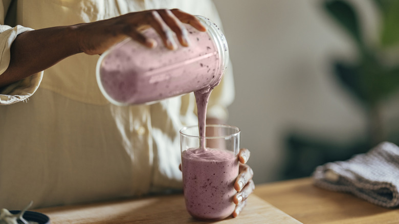 Person pouring fruit smoothie from blender cup to glass