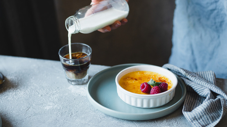 Hand pours milk into coffee next to creme brulee