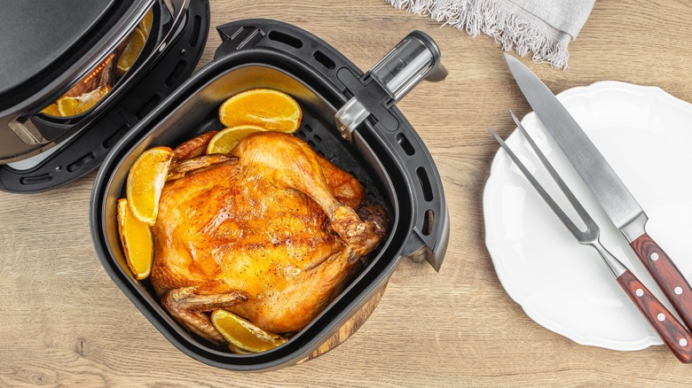 Roasted chicken in an air fryer next to plate with utensils