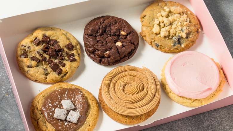 Six crumbl cookies sits in a pink and white bakery box on a stone countertop