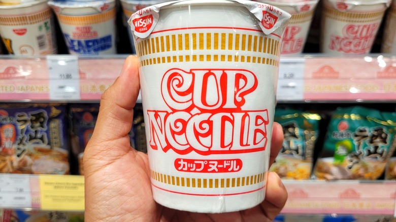 Hand holding Cup Noodles in grocery store