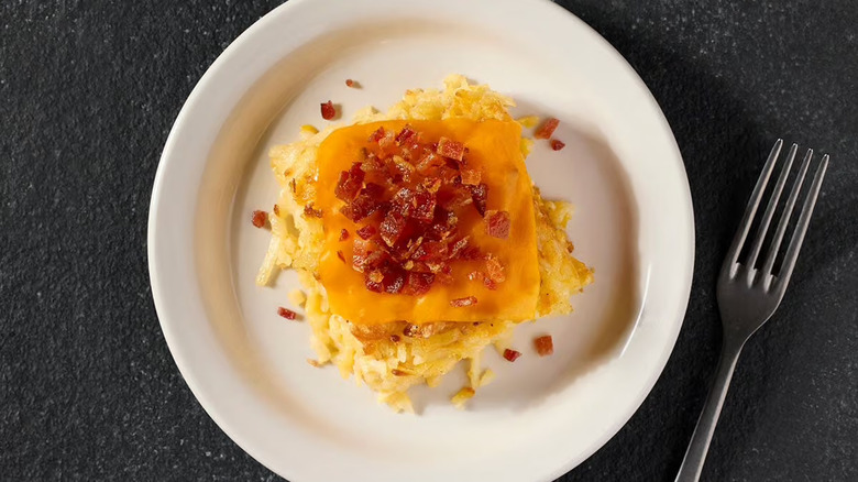 A square of hashbrown casserole sits on a white plate next to a fork