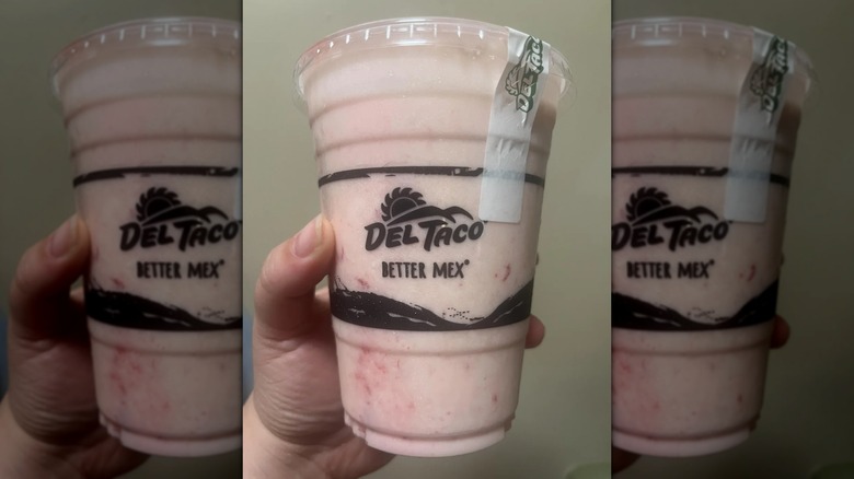 Hand holding a Del Taco strawberry milkshake