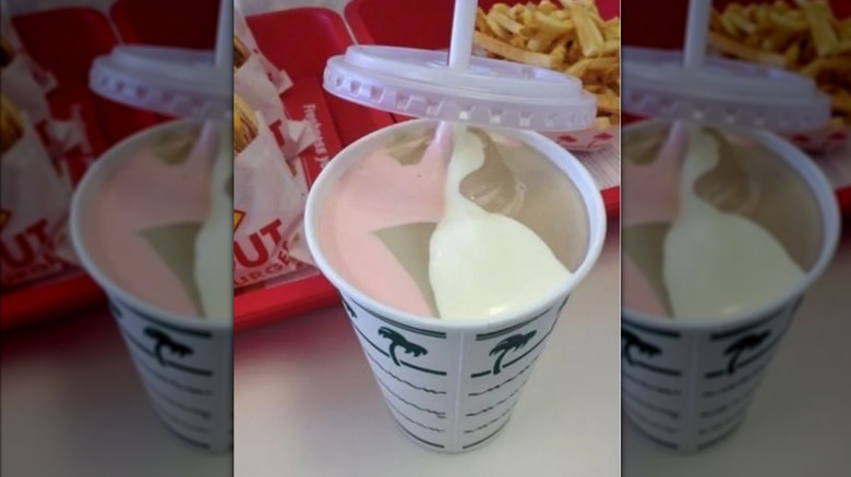 A Neapolitan milkshake on a counter next to a tray of burgers and fries