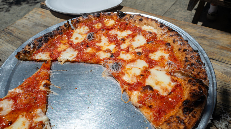 Half of a cheese pizza sits on a silver tray on an outdoor wooden table
