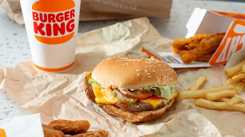 A whopper with cheese is surrounded by fries and chicken fries next to a Burger King soda